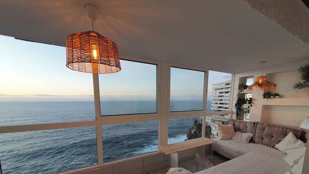 Una camera da letto con un'ampia finestra vista mare, un letto, un comodino e una lampada a sospensione.
