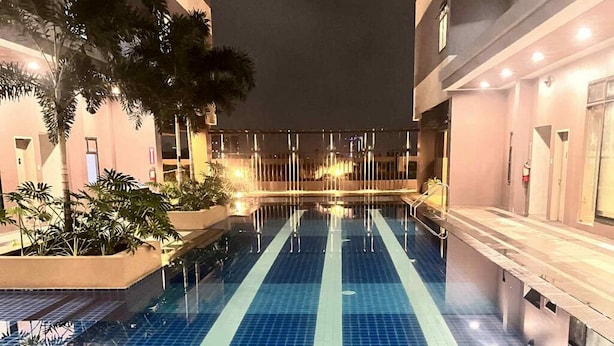 A swimming pool with a tiled floor, surrounded by buildings with balconies and palm trees.