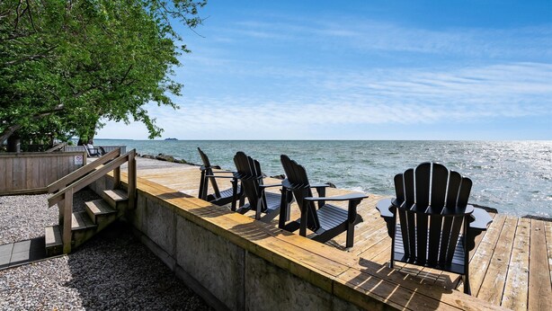 Eine Holzterrasse mit Adirondack-Stühlen mit Blick auf ein Gewässer.