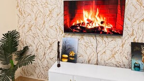 Un saló amb televisió penjada a la paret, un moble blanc, una planta en test i una catifa amb dibuixos.