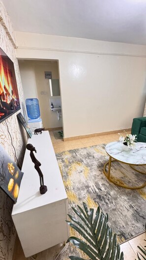 Et værelse med et hvidt skrivebord, et rundt bord med gylden ramme, en vanddispenser og en grøn sofa.