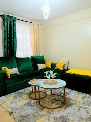 Un salón con un sofá verde, dos mesas redondas y una manta amarilla.