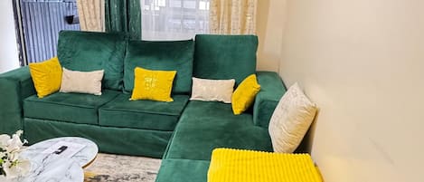 A green sofa with yellow and white cushions, a marble coffee table, and a potted plant.