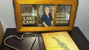 A framed photo with text, a book titled 'Hooker's Lake Camp', a heart-shaped object, and a DVD player with 'The Hunger Games' visible.