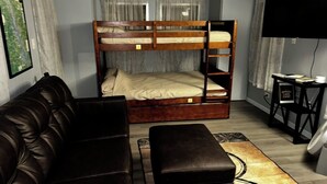 A room with a bunk bed, a leather sofa, a small table, and a TV.