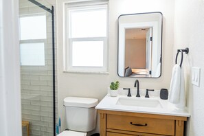 Un baño con un inodoro blanco, un lavabo con un espejo encima, una planta pequeña en maceta y una toalla colgada en la pared.