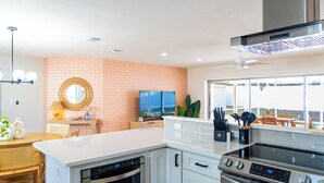 Una cocina moderna con gabinetes blancos, electrodomésticos de acero inoxidable, una pared de acento de ladrillo y un amplio ventanal con vistas a un patio.