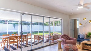 Un salón amplio con un gran ventanal corredera que da a un patio, un sofá rosa, un sofá azul y una mesa de centro de madera.