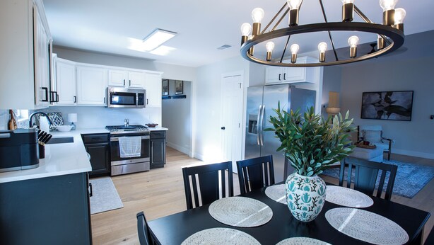 A modern kitchen with white cabinets, a stainless steel stove, and a microwave. There is a dining area with a table and chairs, a vase with plants, and a chandelier. - Charming 3-Bedroom, 2-Bath Home with Office – Just 7 Min to Downtown McKinney! (McKinney)
