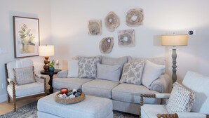 A living room with a sectional sofa, two armchairs, a coffee table with decorative items, a side table with a lamp, and wall art. - Charming 3-Bedroom, 2-Bath Home with Office – Just 7 Min to Downtown McKinney! (McKinney)