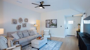 A living room with a sofa, ottoman, and a ceiling fan. There is a door and a lamp on a side table. - Charming 3-Bedroom, 2-Bath Home with Office – Just 7 Min to Downtown McKinney! (McKinney)