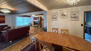 Ein geräumiges Wohnzimmer mit einem Holzesstisch, bequemen Sitzmöglichkeiten, einem Fernseher und dekorativen Wandbildern.