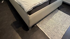 Ein modernes Schlafzimmer mit einem Bett, zwei Kissen, einer Decke, einem Teppich und einem Fenster mit geometrischem Muster.