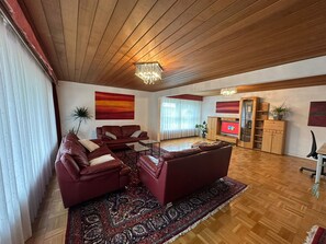 Amplia sala de estar con techo de madera, un gran sofá rojo, una mesa de centro, un televisor y un mueble de madera con estantes.