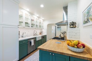A modern kitchen with teal cabinets, a wooden countertop, and a fruit bowl.