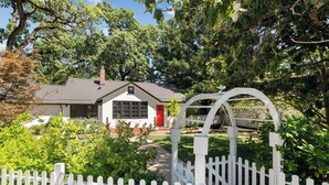 Een huis met een witte picket fence, een rode deur en een tuin met diverse planten.