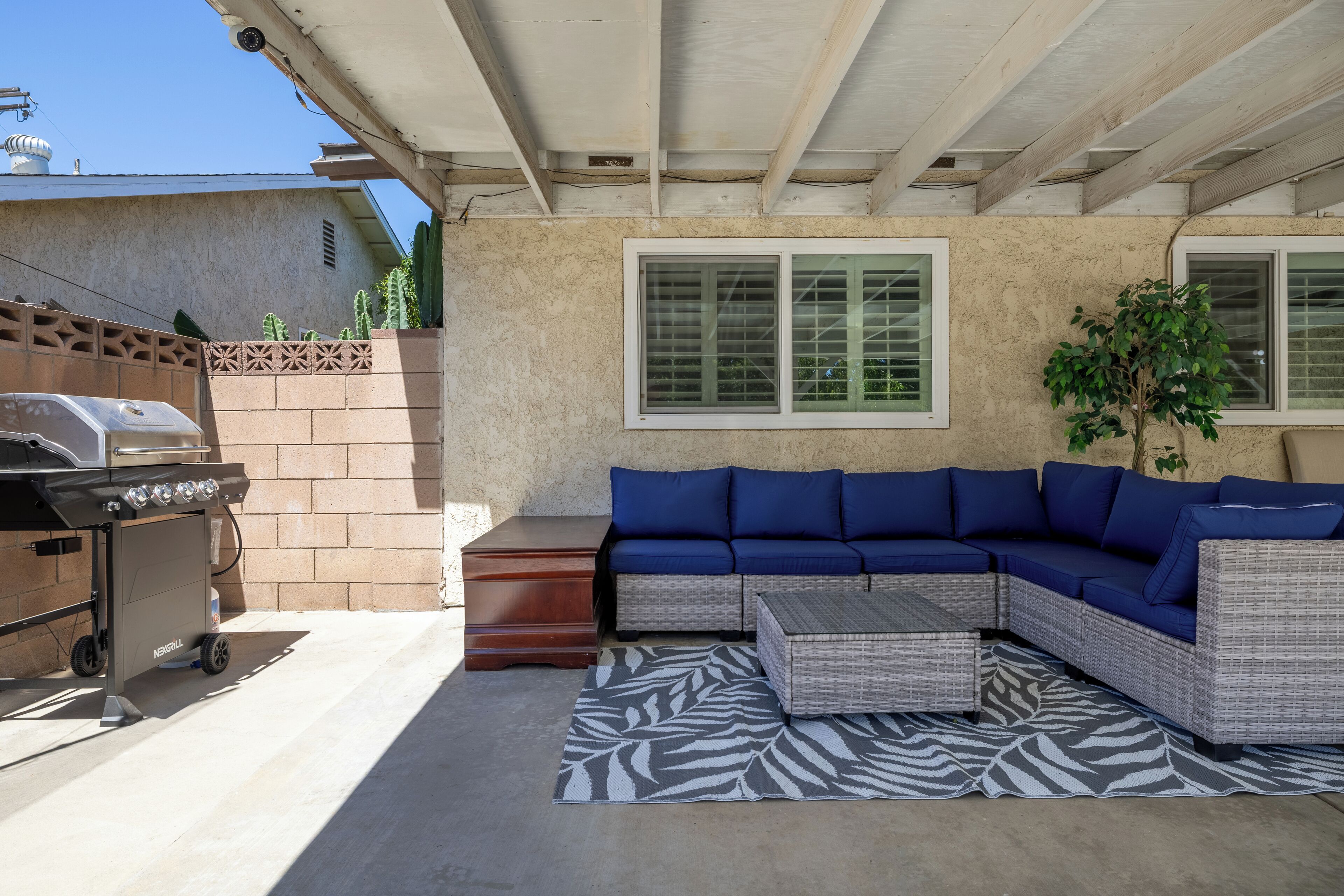 Une terrasse extérieure avec un canapé d’angle, un barbecue et un tapis à motifs zébrés.