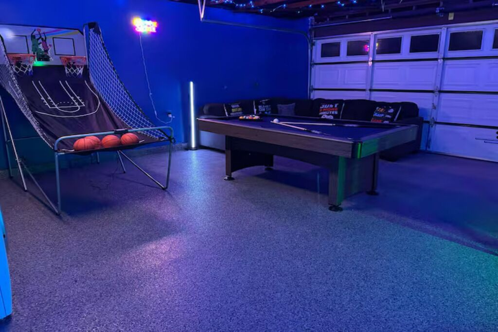 A pool table with a basketball hoop and a sofa in a room with a garage door.