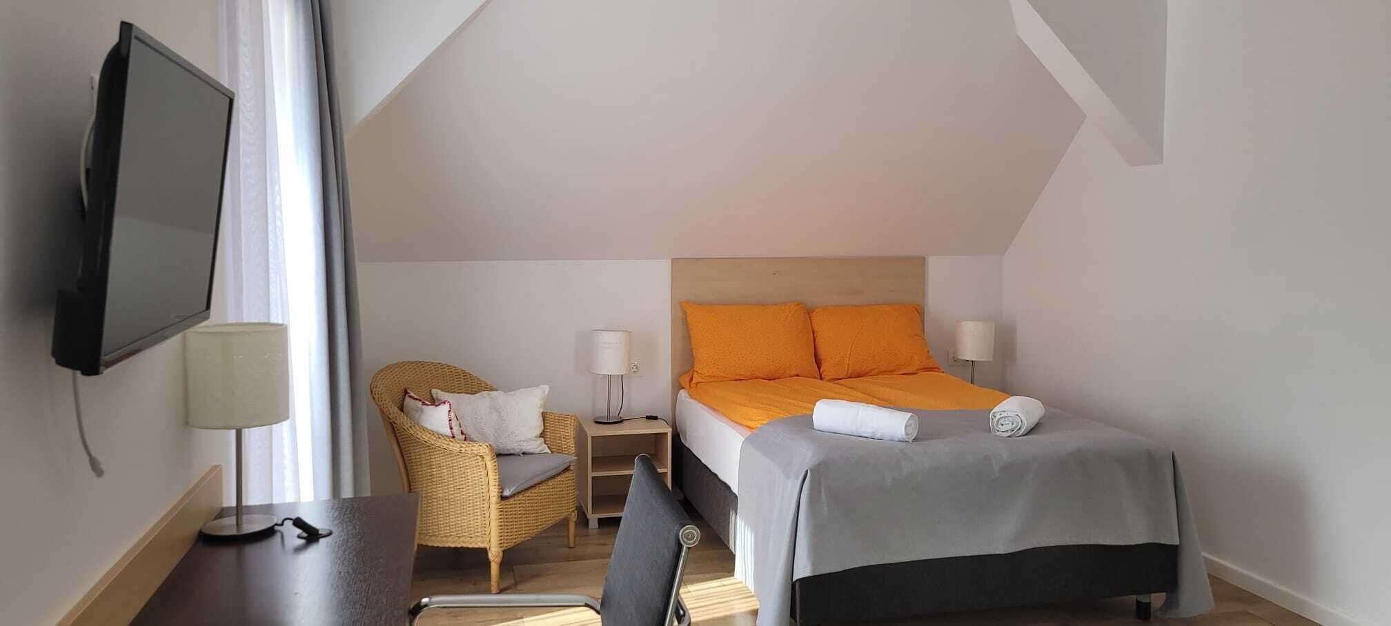 A hotel room with a bed, a chair, a TV, and a lamp.