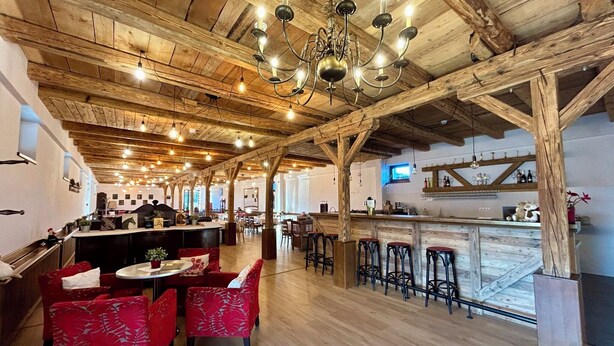 A rustic interior with exposed wooden beams, a bar area, and red upholstered chairs. - Sólyom Major - Gut Falkenhof (Sacel)