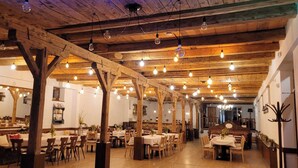 A restaurant with wooden beams, hanging light bulbs, and tables set for dining.