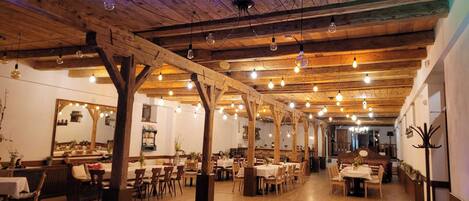 A restaurant with wooden beams, hanging light bulbs, and tables set for dining.
