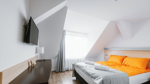 A modern hotel room with a bed, bedside table, and a flat-screen TV mounted on the wall.