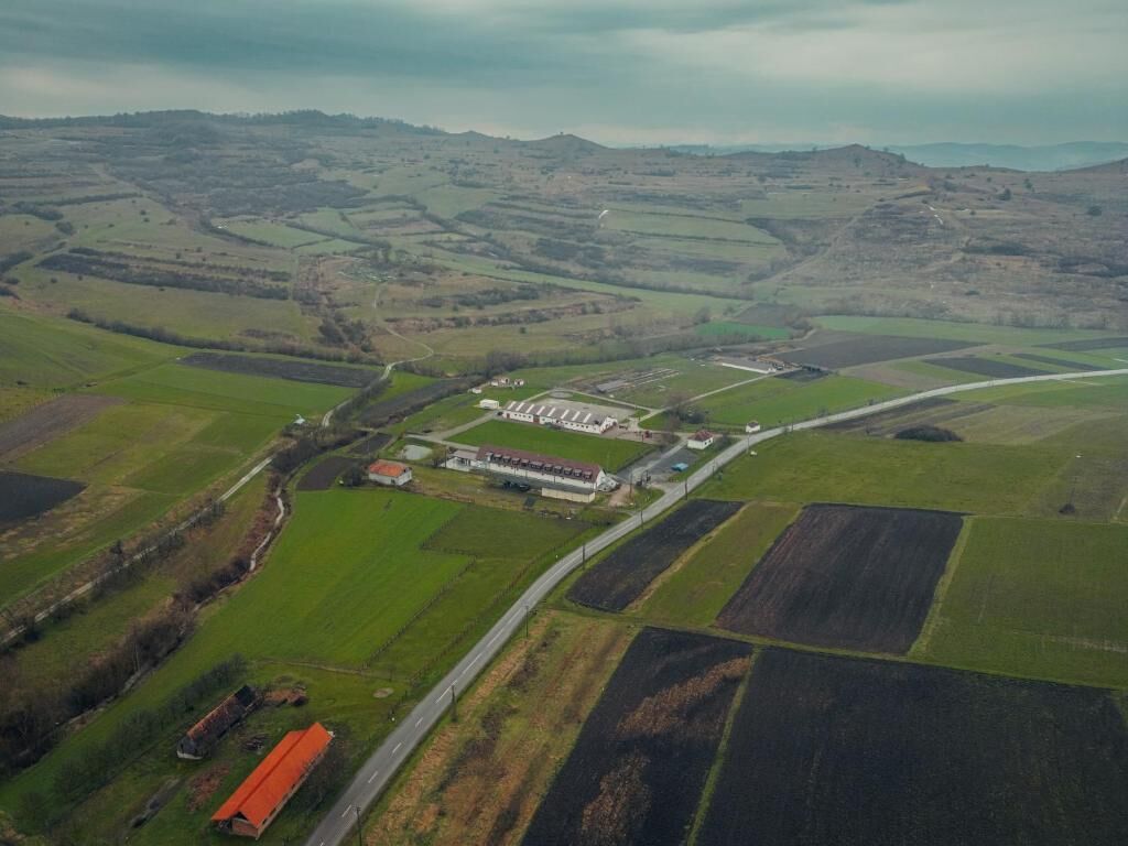 An aerial view of a rural landscape with fields, a road, and a large building with a red roof.