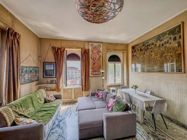 A cozy living room with a sofa, a dining table, and a large painting on the wall. - Perfectly located in the heart of Rome, transportation right outside your door (Roma)