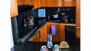 A kitchen with wooden cabinets, a black countertop, a coffee maker, a kettle, and a sink. - Perfectly located in the heart of Rome, transportation right outside your door (Roma)