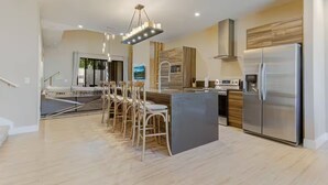 A modern kitchen with a central island, stainless steel appliances, and a bar area with chairs. - Fantasy Disney Home 45858326 (Kissimmee)