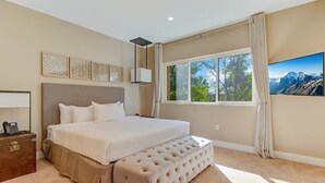 A bedroom with a large bed, a bedside table with a phone, a window with a mountain view, and a painting on the wall. - Fantasy Disney Home 45858326 (Kissimmee)