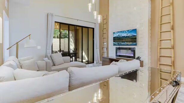A modern living room with a glass coffee table, a sofa set, a TV mounted on the wall, and a ladder leaning against the wall. - Fantasy Disney Home 45858326 (Kissimmee)