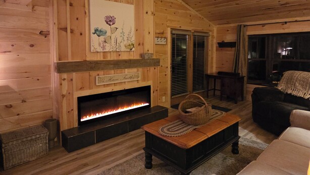 Ein gemütliches Blockhauss-Interieur mit Holzausstattung, Kamin, einer Couch und einem Essbereich.