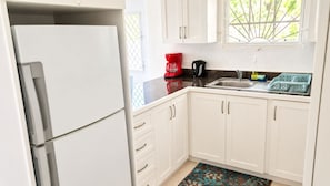Una cocina con armarios blancos, un refrigerador, una cafetera y un ventanal con vistas a zonas verdes.