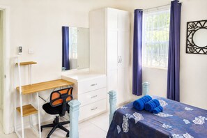 A bedroom with a desk, chair, wardrobe, and a bed with rolled towels.