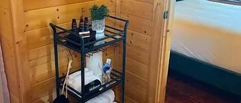 A wooden cabin room with a bed, a small shelf with toiletries, and a window.