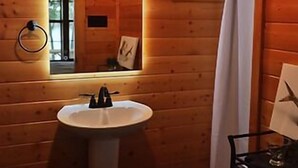 Une salle de bain rustique, avec des murs en bois, comprenant un lavabo, un miroir et un rideau de douche.