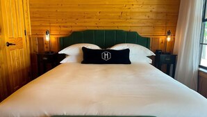 Un lit bien fait, avec une tête de lit verte et du linge de lit blanc, deux tables de chevet avec des lampes et un mur lambrissé en bois.