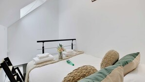 Een net opgemaakt bed met een geweven deken, een kleine vaas met bloemen en keurig gevouwen handdoeken.
