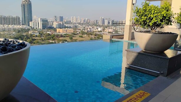 An infinity pool with a city view, a potted plant, and a yellow safety sign. - High rise apartments (Gurugram)