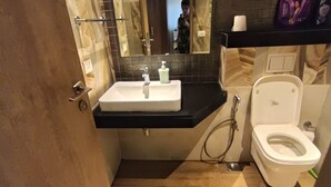 A bathroom with a white sink, a toilet, and a shower area. - High rise apartments (Gurugram)