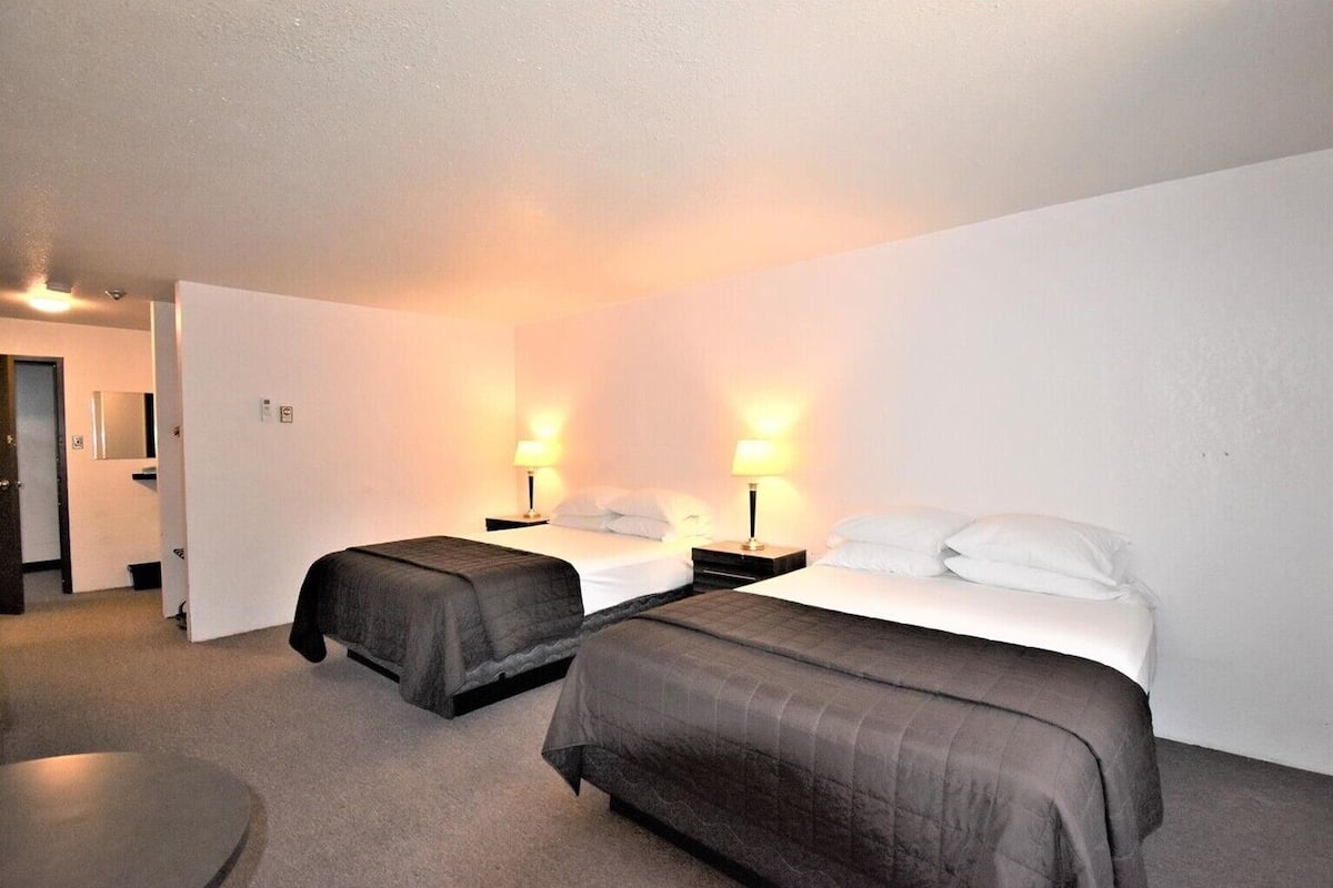 A hotel room with two single beds, a small round table, and a door leading to a bathroom.