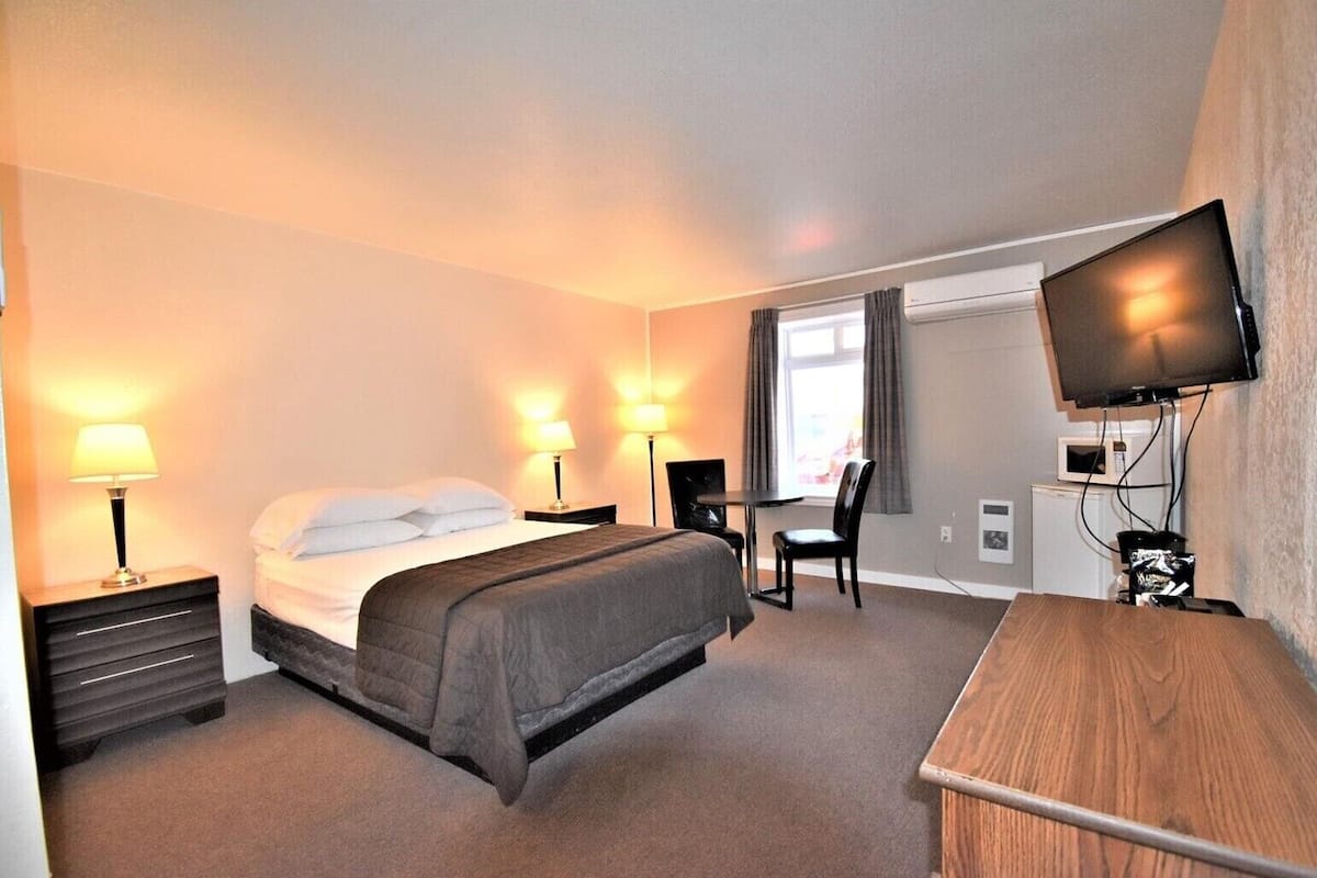A hotel room with a bed, bedside lamps, a desk with a chair, a television, and a microwave.