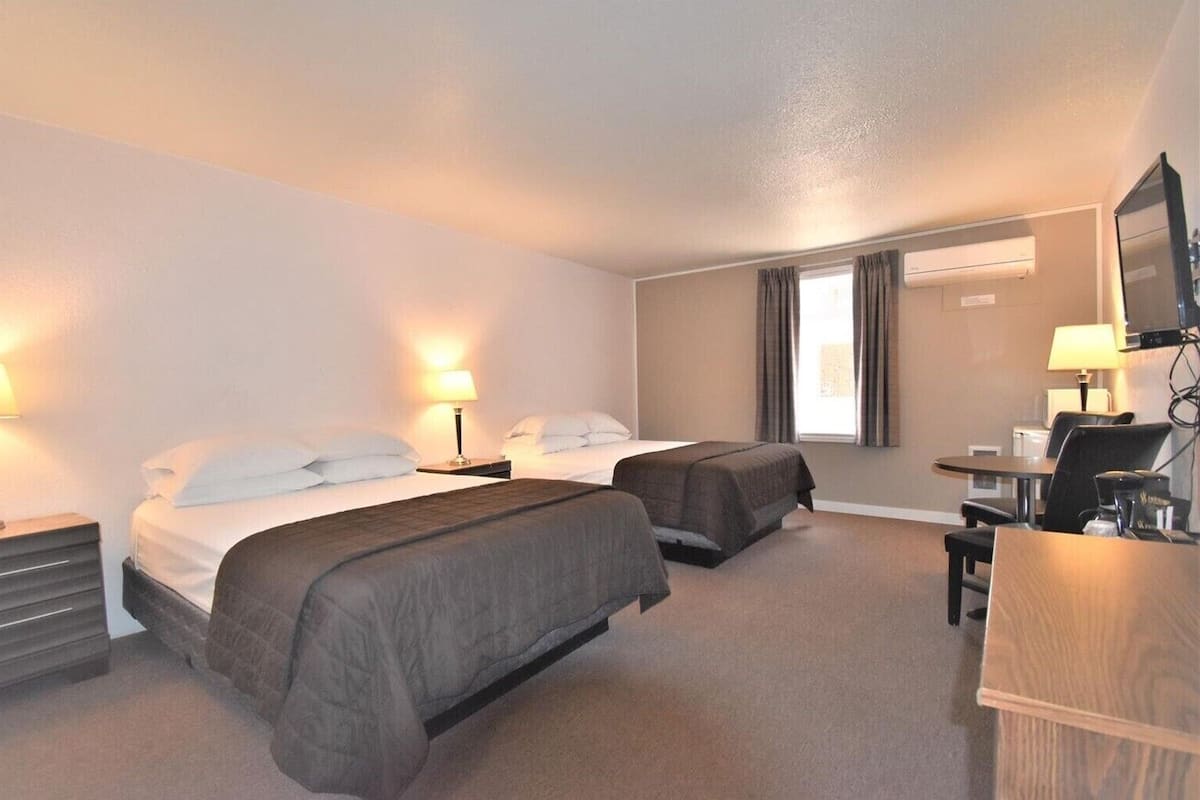 A hotel room with two beds, a desk, a chair, a TV, and a window with curtains.