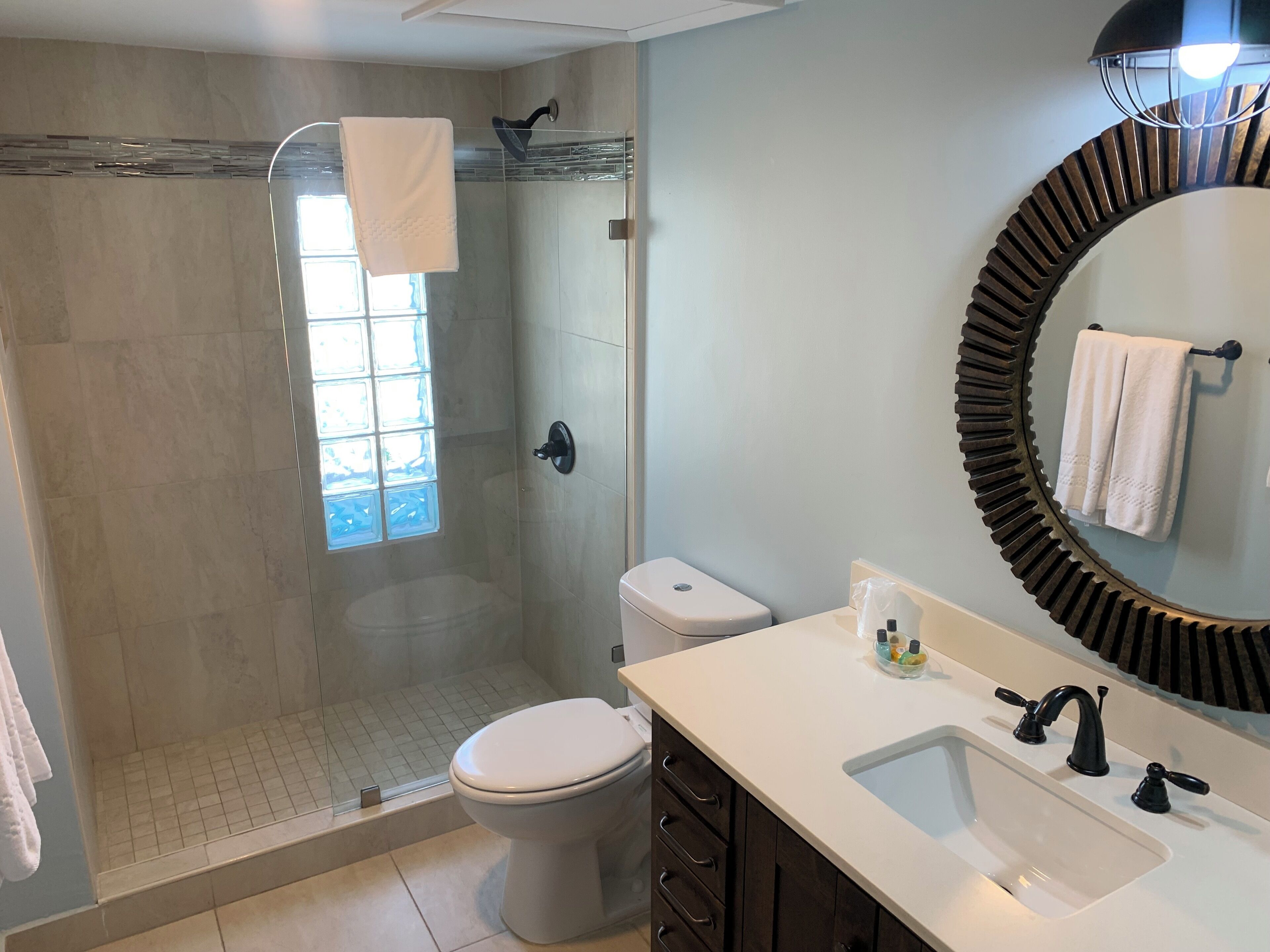 A modern bathroom with a glass-enclosed shower, a toilet, and a sink with a mirror.