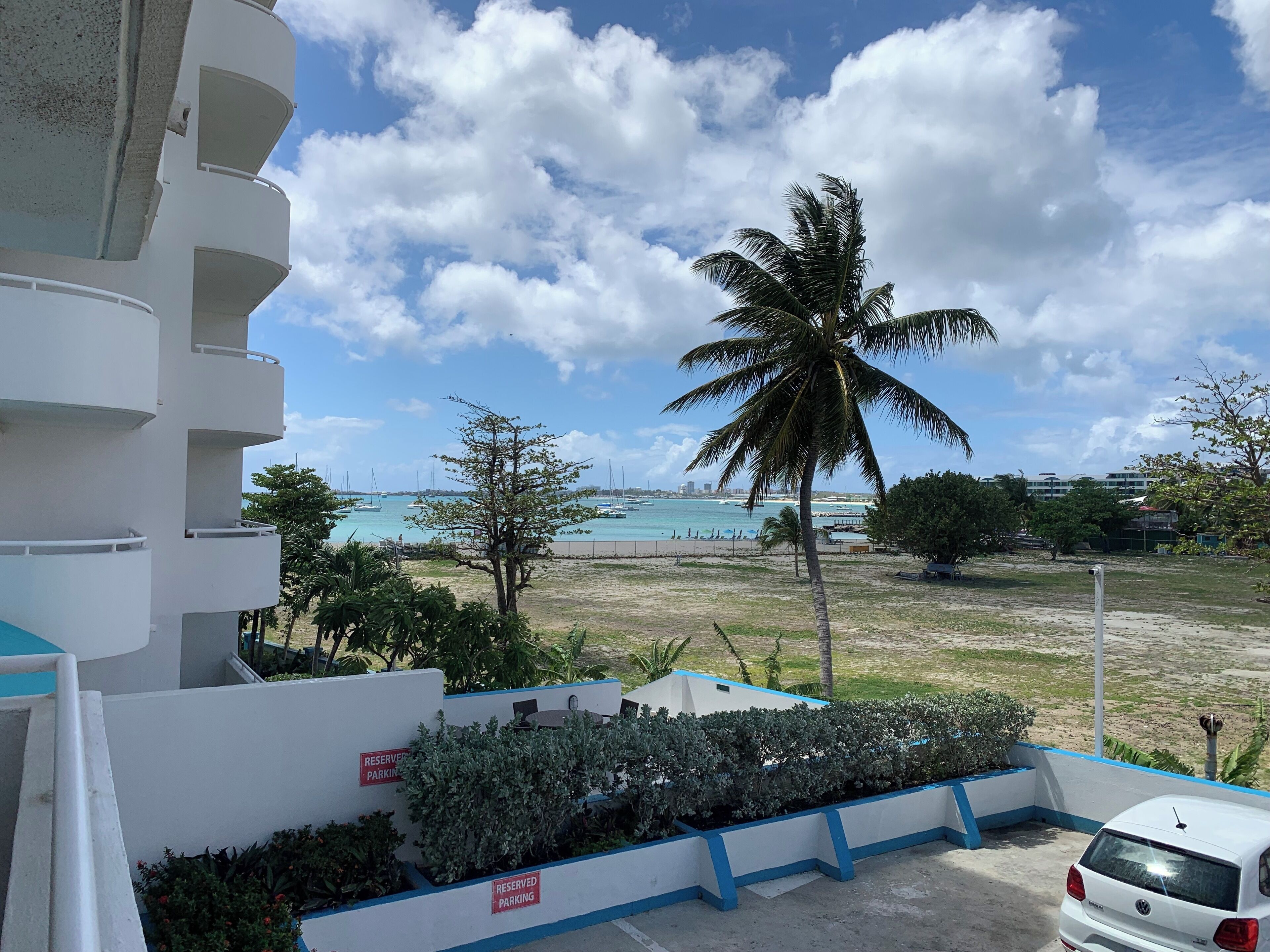 Une vue d’une plage avec un bâtiment blanc au premier plan, un palmier et un ciel dégagé.