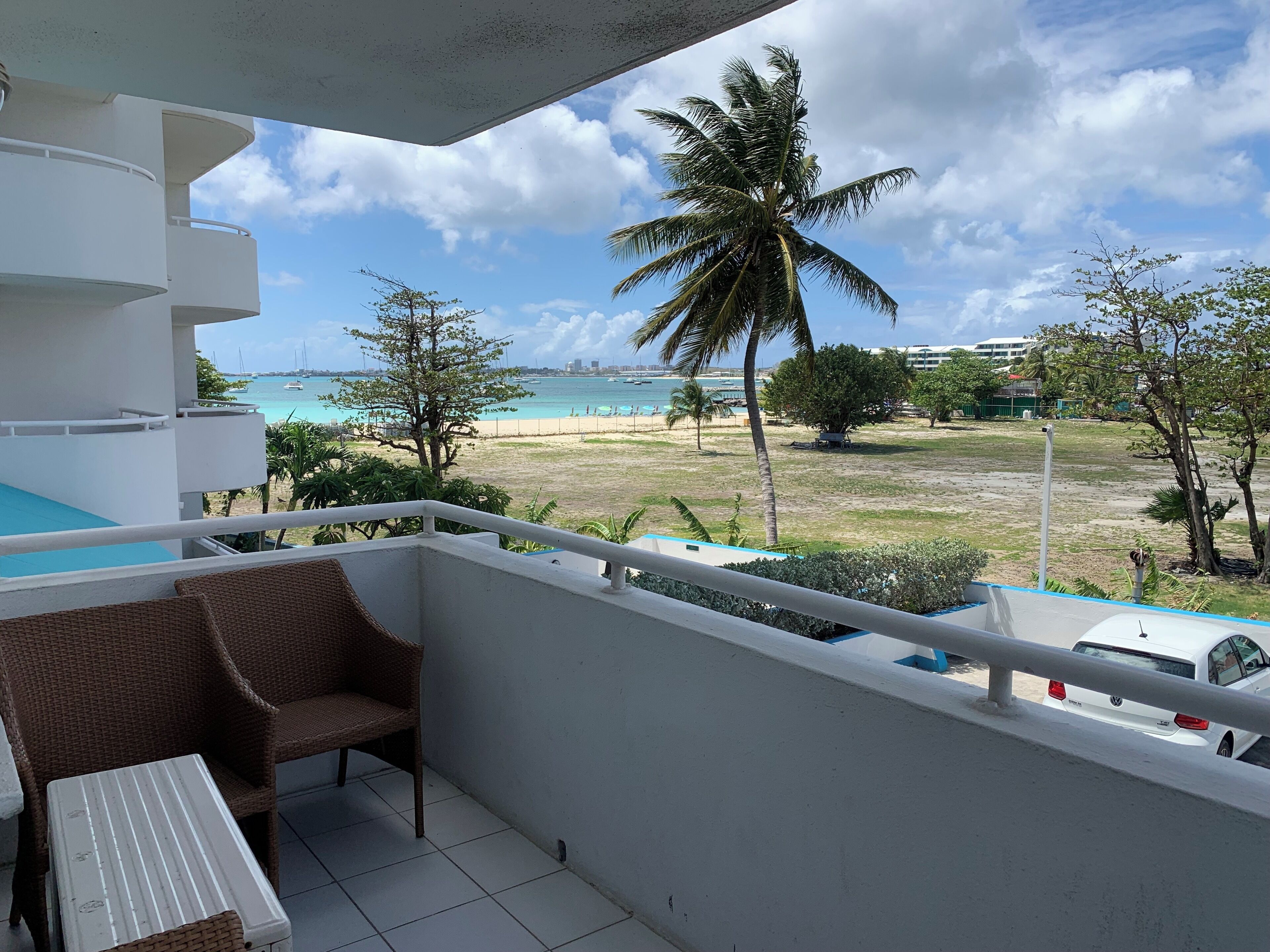 Ein Balkon mit Blick auf den Strand, ein weißes Auto und eine Palme.