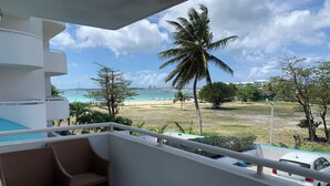 En balkon med udsigt over stranden, en hvid bil og en palme.