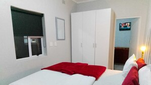 A bedroom with a bed, a wardrobe, a television, and a window with a blind. - Neo & Ruks Guest House Parow (Cape Town)